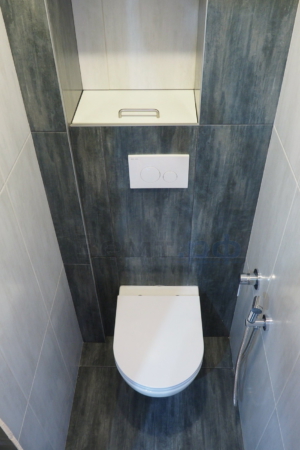 Туалет с уложенной плиткой, установленной инсталляцией и гигиеническим душем