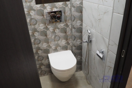 Отремонтированный туалет с подвесным унитазом, рядом висят гигиеническим душем и держателем бумаги